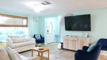 Un salon comprenant un canapé, des fauteuils, une table basse, un téléviseur et un meuble.