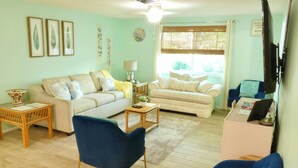 A living room with two sofas, a blue chair, a TV, and a window with blinds. - Private 2BR/2BA Home: Saltwater Pool, Fenced Yard, Sleeps 6 -Custom winter rates (Port Richey)