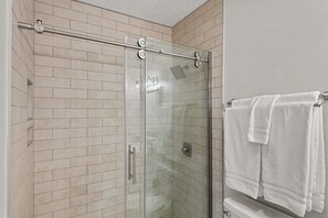 Une douche fermée par des parois en verre, dotée d’une poignée en métal et d’un porte-serviettes avec deux serviettes blanches.