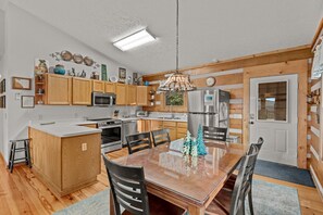 Une cuisine moderne avec des meubles en bois, des appareils en acier inoxydable et un coin repas comprenant une table et des chaises en verre.