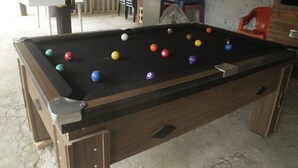 Un tavolo da biliardo con le palle, una parete in mattoni e una panca di legno sullo sfondo.