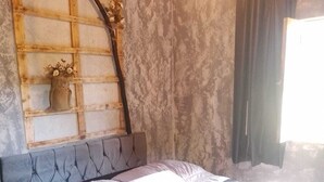 Una camera da letto con un letto, una testiera in legno, una mensola a parete con un vaso e una finestra con tende.