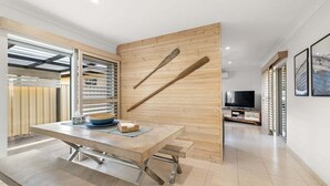 A modern dining area with a wooden wall, a television, and a dining table with benches. - Pet Friendly Beachside Hideaway - Lazy on Lowry (WOORIM)