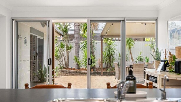 A modern kitchen with a view of a patio area featuring palm trees and a brick wall. - Pet Friendly Beachside Hideaway - Lazy on Lowry (WOORIM)