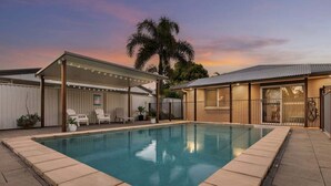A swimming pool with a covered patio area, a fenced backyard, and a house with a metal roof. - Pet Friendly Beachside Hideaway - Lazy on Lowry (WOORIM)