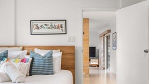 A hotel room with a bed, pillows, a framed artwork, and a television in the background. - Pet Friendly Beachside Hideaway - Lazy on Lowry (WOORIM)