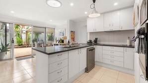 A modern kitchen with white cabinets, a dishwasher, and a large island with a sink. - Pet Friendly Beachside Hideaway - Lazy on Lowry (WOORIM)