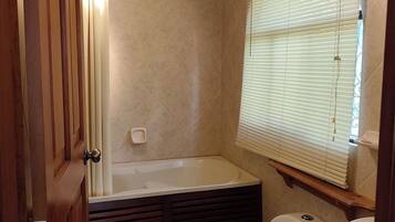 Ein Badezimmer mit Badewanne, Toilette und Fenster mit Jalousien.