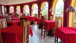 A restaurant with red tablecloths, wooden chairs, and arched windows.
