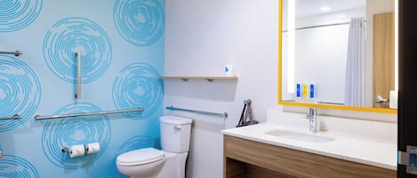 Un baño moderno con un motivo circular azul en la pared, un inodoro blanco, un tocador de madera con espejo y un lavabo.