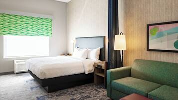 Habitación de hotel con cama, sofá verde, mesita de noche, lámpara y un cuadro en la pared.