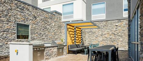 An outdoor patio with a stone wall, a barbecue grill, and a seating area with a table and chairs.
