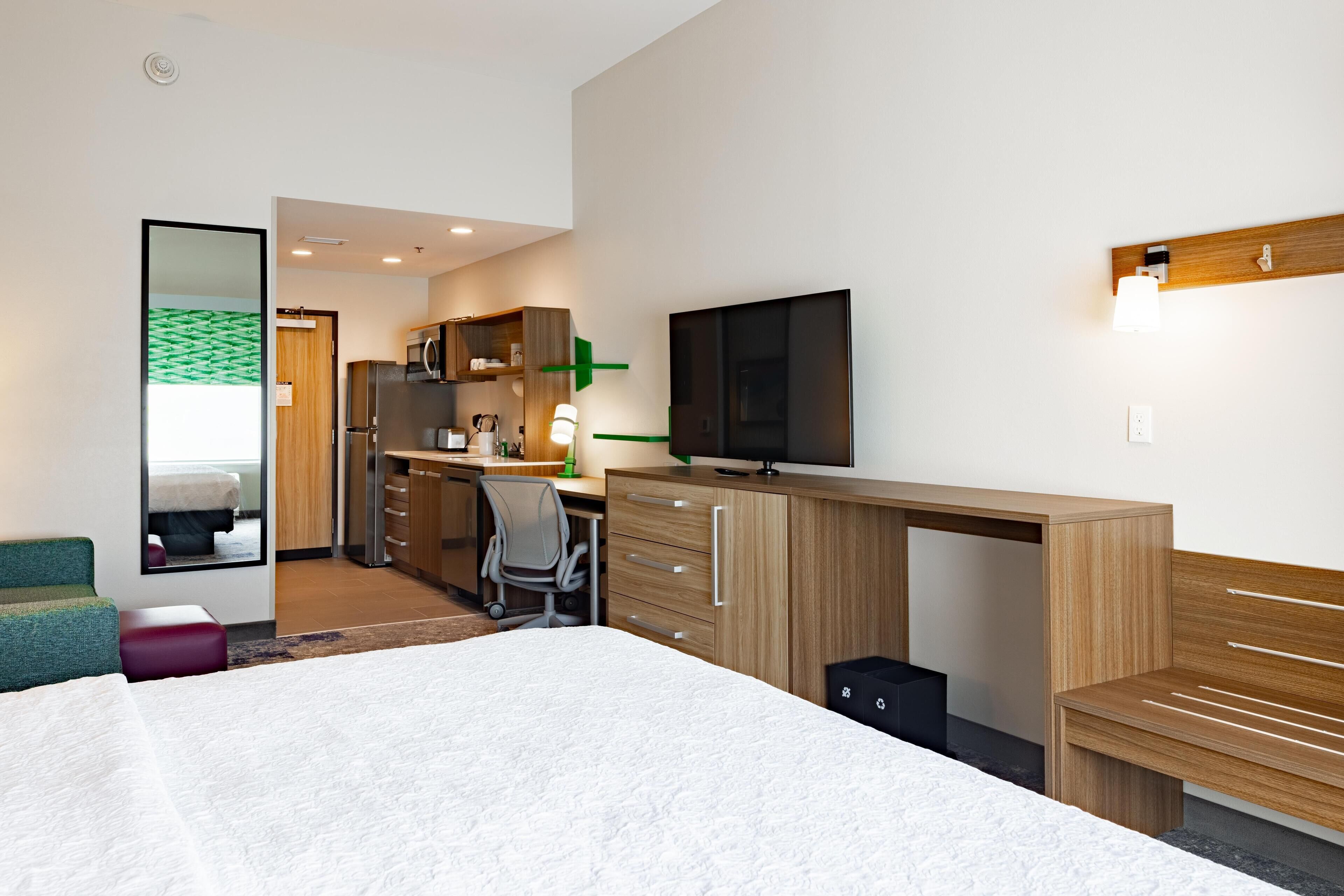 A modern hotel room with a large bed, a desk with a flat-screen TV, a mirror, and a wardrobe.