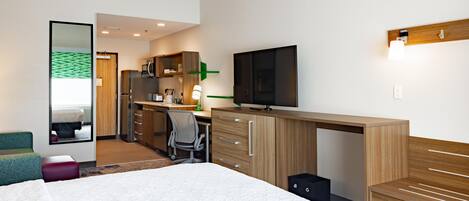 A modern hotel room with a large bed, a desk with a flat-screen TV, a mirror, and a wardrobe.