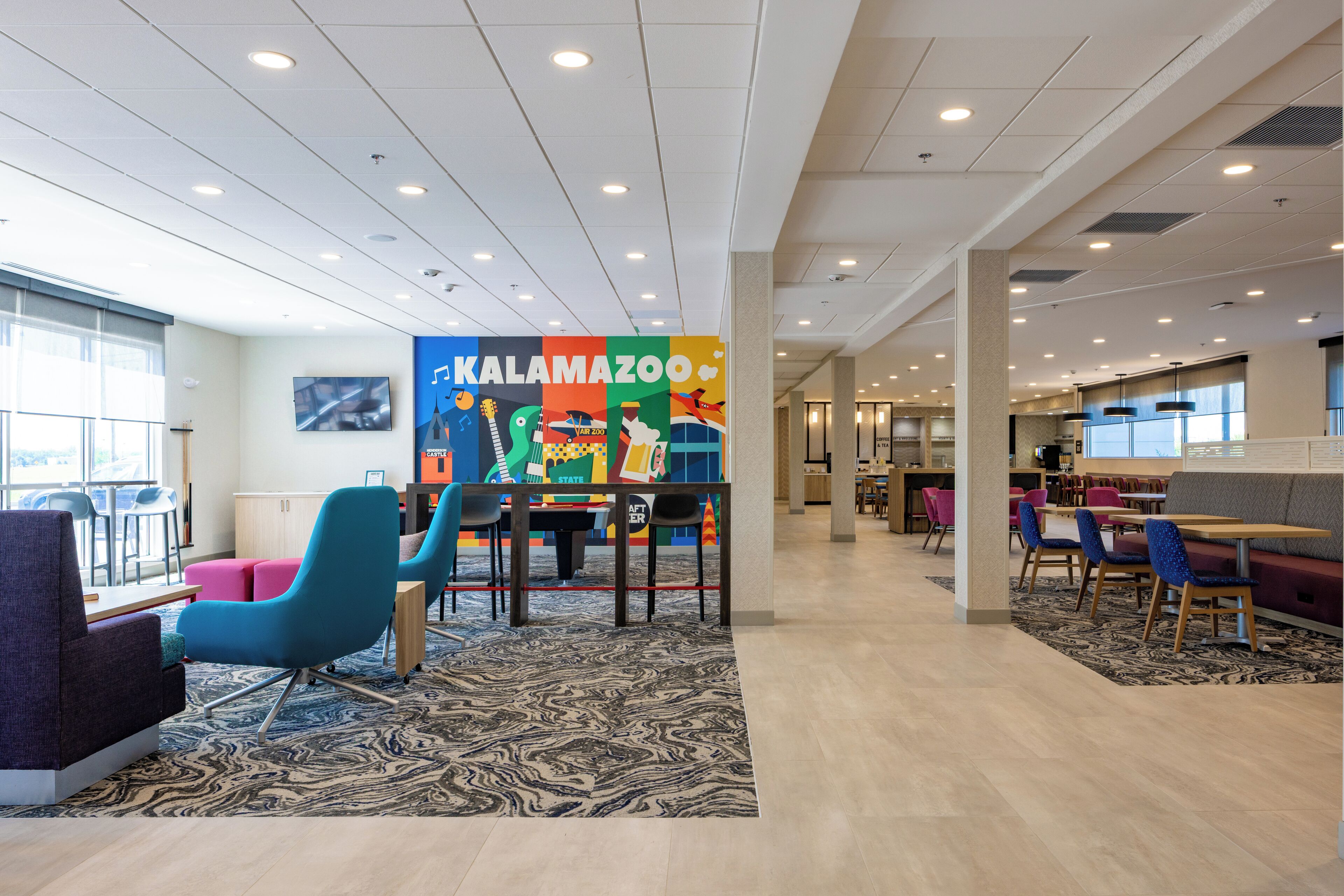 A spacious indoor area with a colorful mural, modern seating, and a mix of tables and chairs.