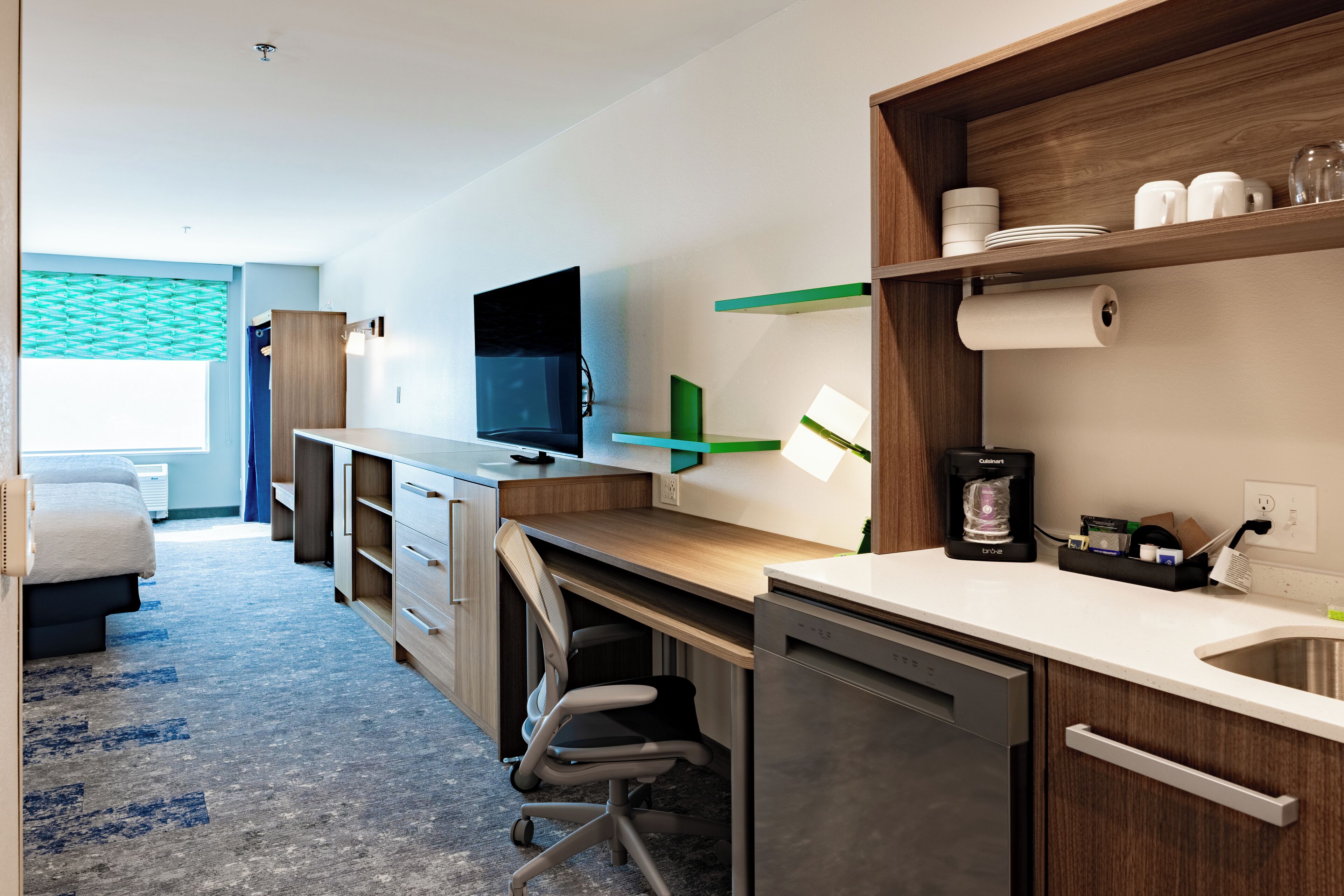 Une chambre d’hôtel moderne équipée d’une kitchenette, d’un téléviseur à écran plat, d’un bureau et d’un lit.