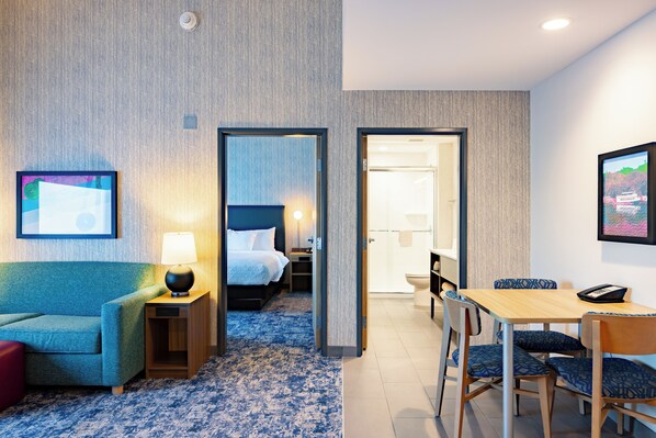 A hotel room with a bed, a desk, a chair, a lamp, and a painting on the wall.