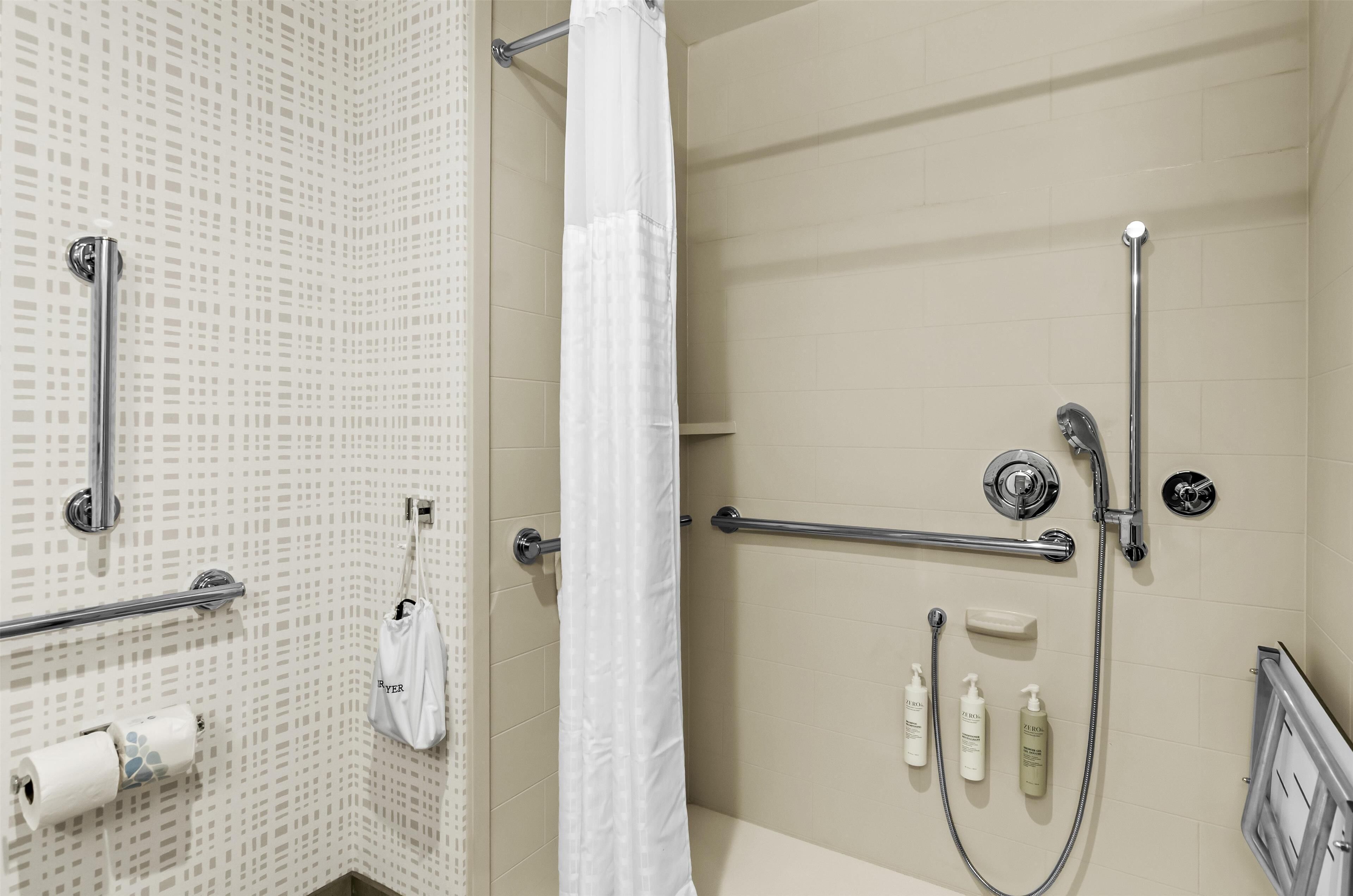 A shower area with a handrail, a white shower curtain, and a towel rack.