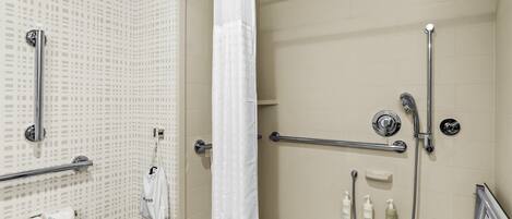 A shower area with a handrail, a white shower curtain, and a towel rack.