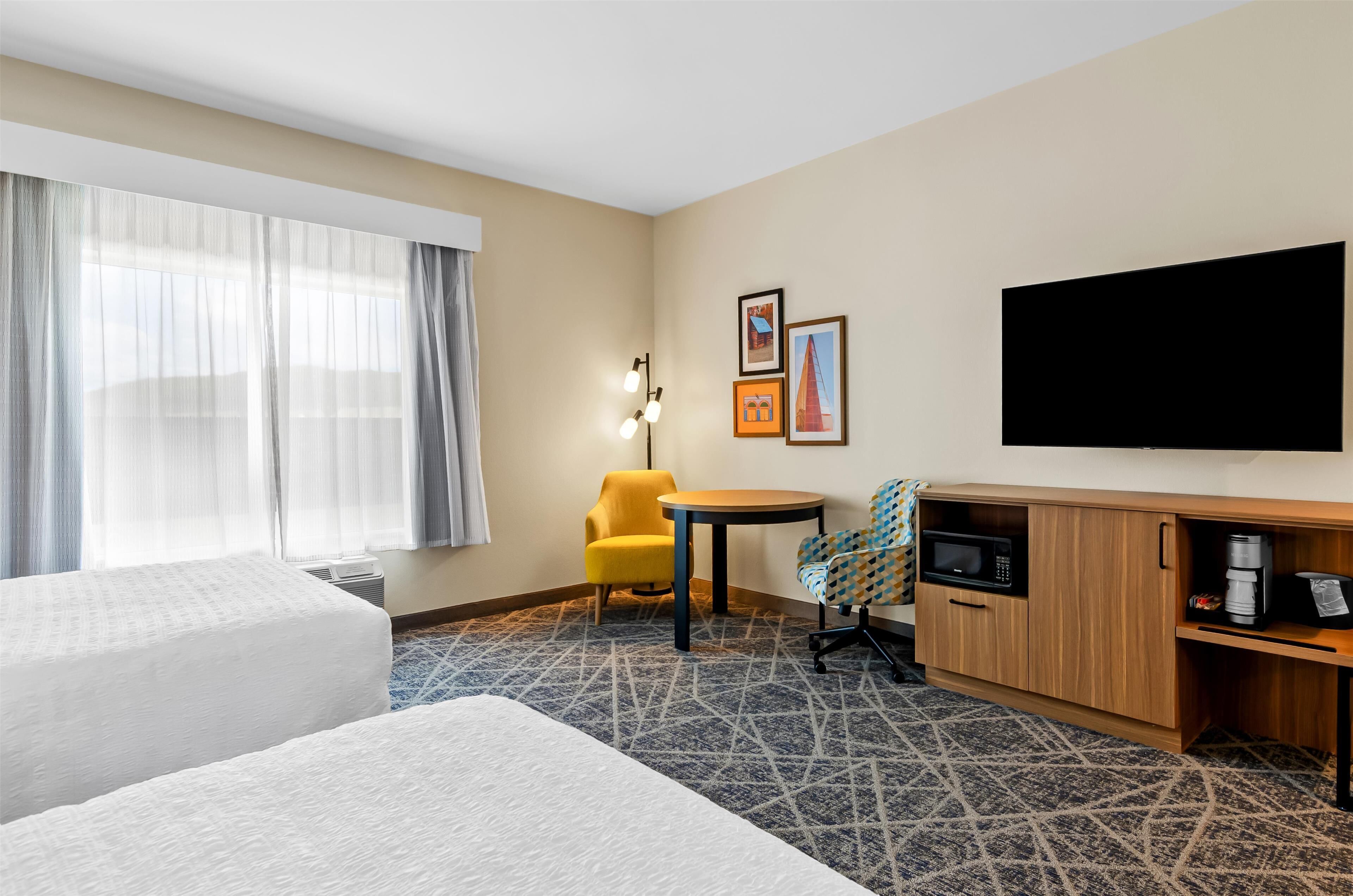 Une chambre d’hôtel avec deux lits, un bureau, une chaise, un téléviseur à écran plat et une machine à café.