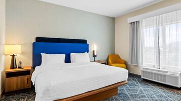 A hotel room with a large bed, a bedside table with a lamp, a chair, and a window with curtains.