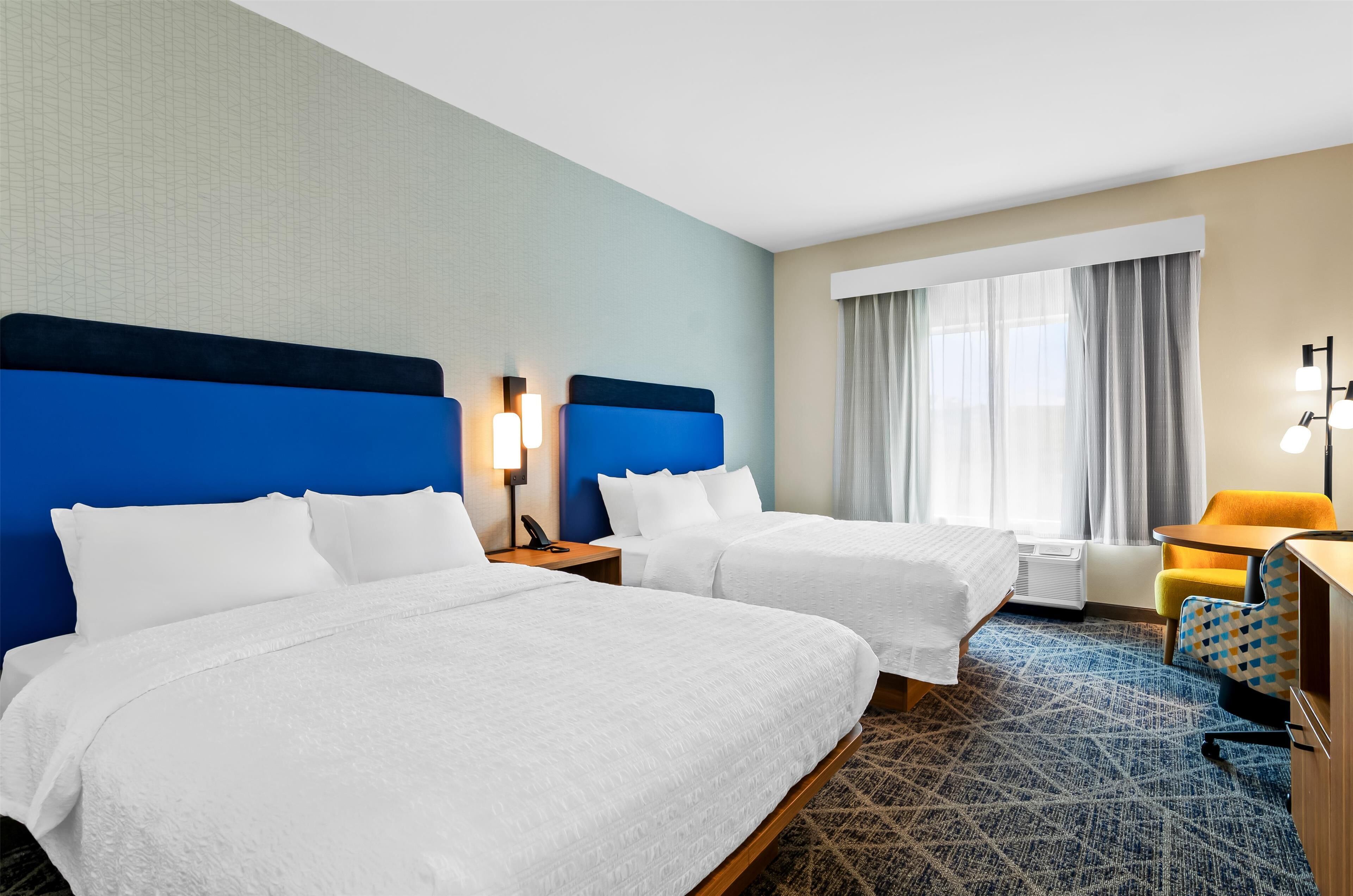 A hotel room with two beds, a desk, a chair, and a window with curtains.