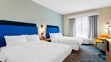 A hotel room with two beds, a desk, a chair, and a window with curtains.