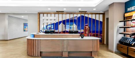 A hotel reception area with a 'Welcome to Hampton' sign, a reception desk, and a 'Welcome' mat.