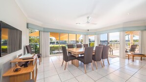 A spacious dining area with a large table and chairs, large windows with curtains, and a view of the outdoors. - Spacious Canal Home With Pontoon! (BANKSIA BEACH)