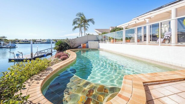 A swimming pool with clear water, surrounded by a stone deck and a glass enclosure with chairs. - Spacious Canal Home With Pontoon! (BANKSIA BEACH)