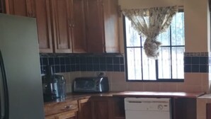 Een keuken met houten kastjes, een vaatwasser, een broodrooster en een raam met gordijn.
