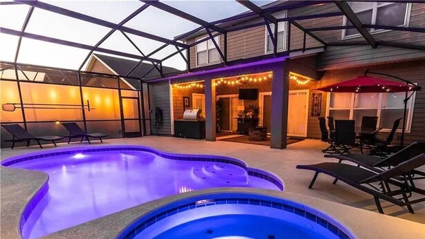 Un área de piscina con dos jacuzzis, sillas de descanso y un patio cubierto con luces colgantes.