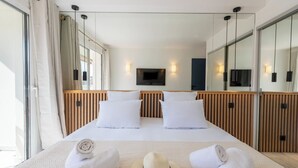 Une chambre d’hôtel avec un grand lit, une tête de lit en bois, un téléviseur à écran plat fixé au mur et une grande fenêtre avec des rideaux.
