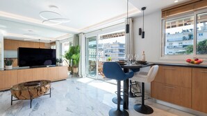 Une cuisine moderne dotée d’un grand téléviseur, d’un coin repas avec des chaises et offrant une vue sur les bâtiments à travers de grandes fenêtres.