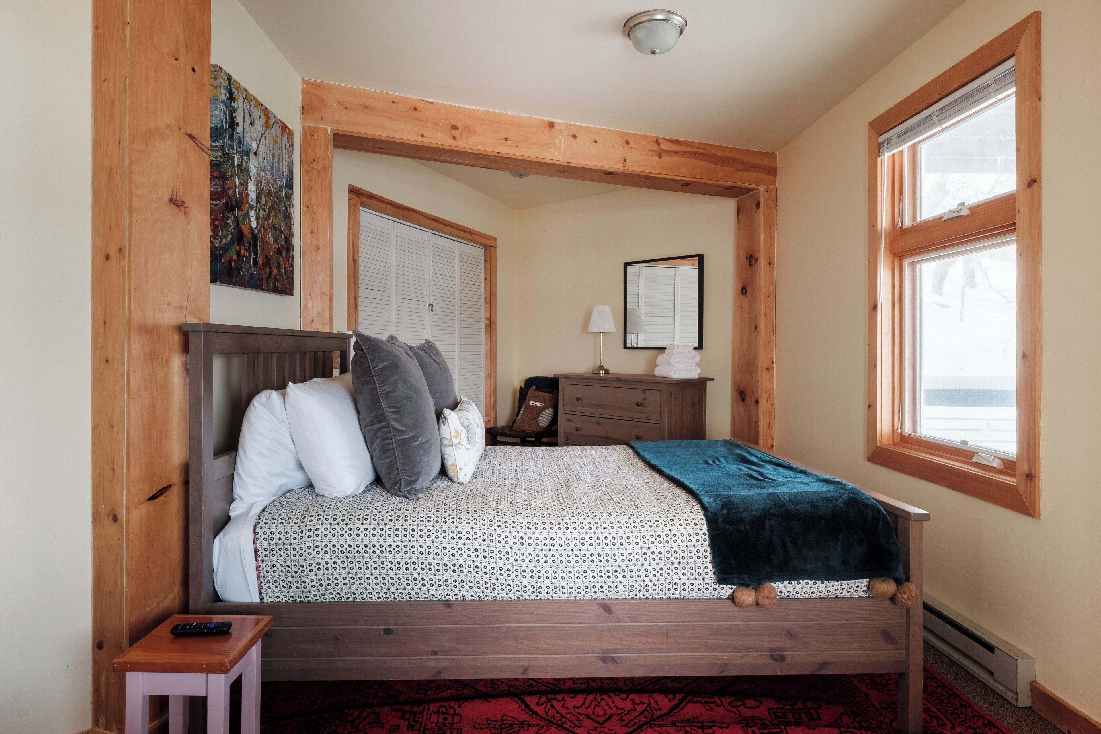 A bedroom with a wooden bed, a nightstand, a dresser, and a window with a view.