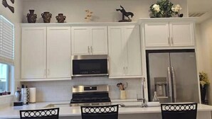 Una cucina moderna con mobili bianchi, elettrodomestici in acciaio inossidabile e oggetti decorativi sugli scaffali.