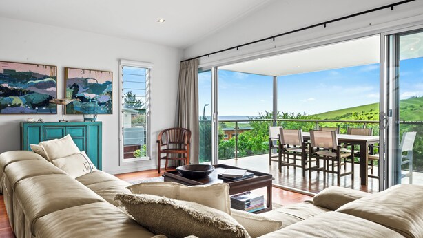 Un salon spacieux avec un grand canapé, une table basse et une vue sur un balcon aménagé avec du mobilier d’extérieur.