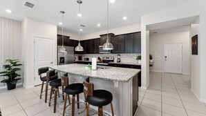 A modern kitchen with a central island, bar stools, pendant lighting, and dark cabinetry. - The Fairytale Escape 5BD Pool BBQ and Resort Access (Davenport)