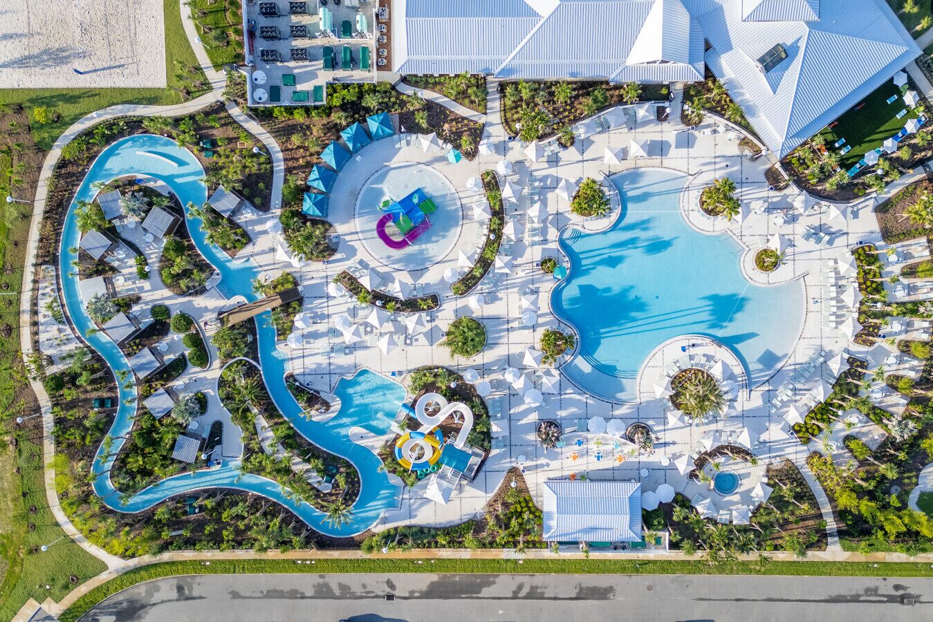 An aerial view of a resort with a large central pool, multiple smaller pools, and a winding water slide.