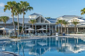 A hotel with a swimming pool, palm trees, and a covered outdoor seating area.