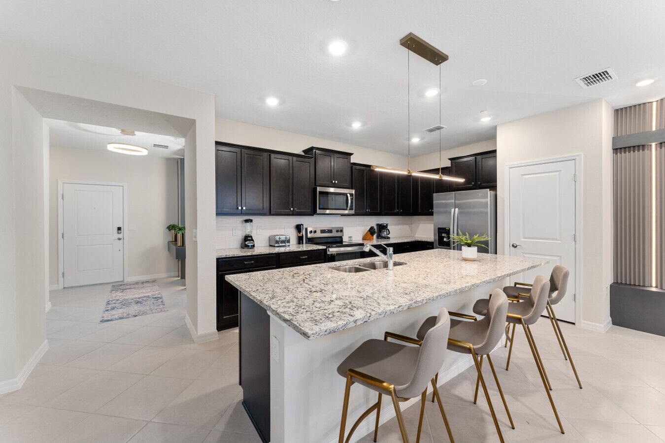 A modern kitchen with dark cabinets, a large island with bar stools, stainless steel appliances, and pendant lighting.