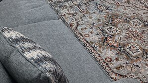 A living room with a grey sectional sofa, a patterned rug, and a dining area with a table and chairs.