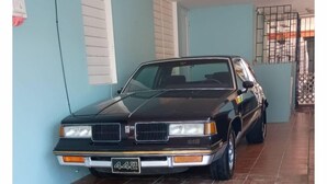 A black car parked in a covered area with tiled flooring and light blue walls.