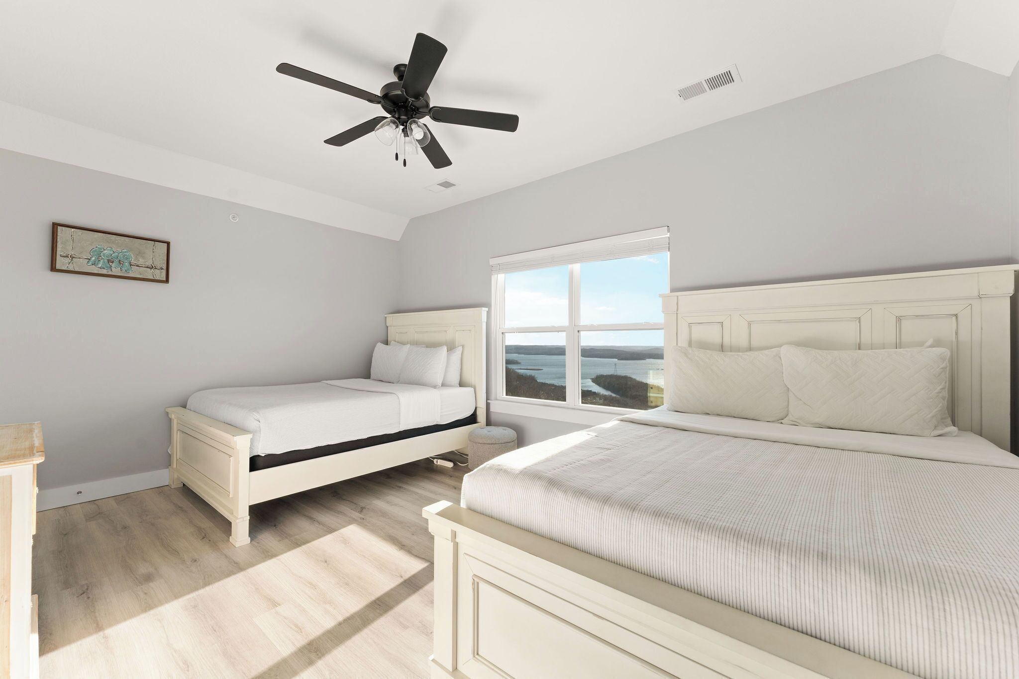 A bedroom with two beds, a ceiling fan, a window with a view, and a small bedside table.