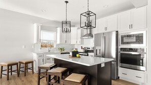 Cocina moderna con armarios blancos, electrodomésticos de acero inoxidable, una isla grande con taburetes e iluminación colgante.