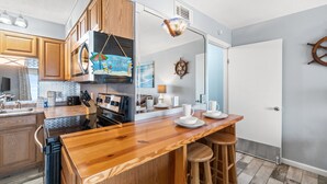 Una cocina moderna con armarios de madera, una isla central con taburetes, un microondas y un adorno con forma de timón de barco en la pared.