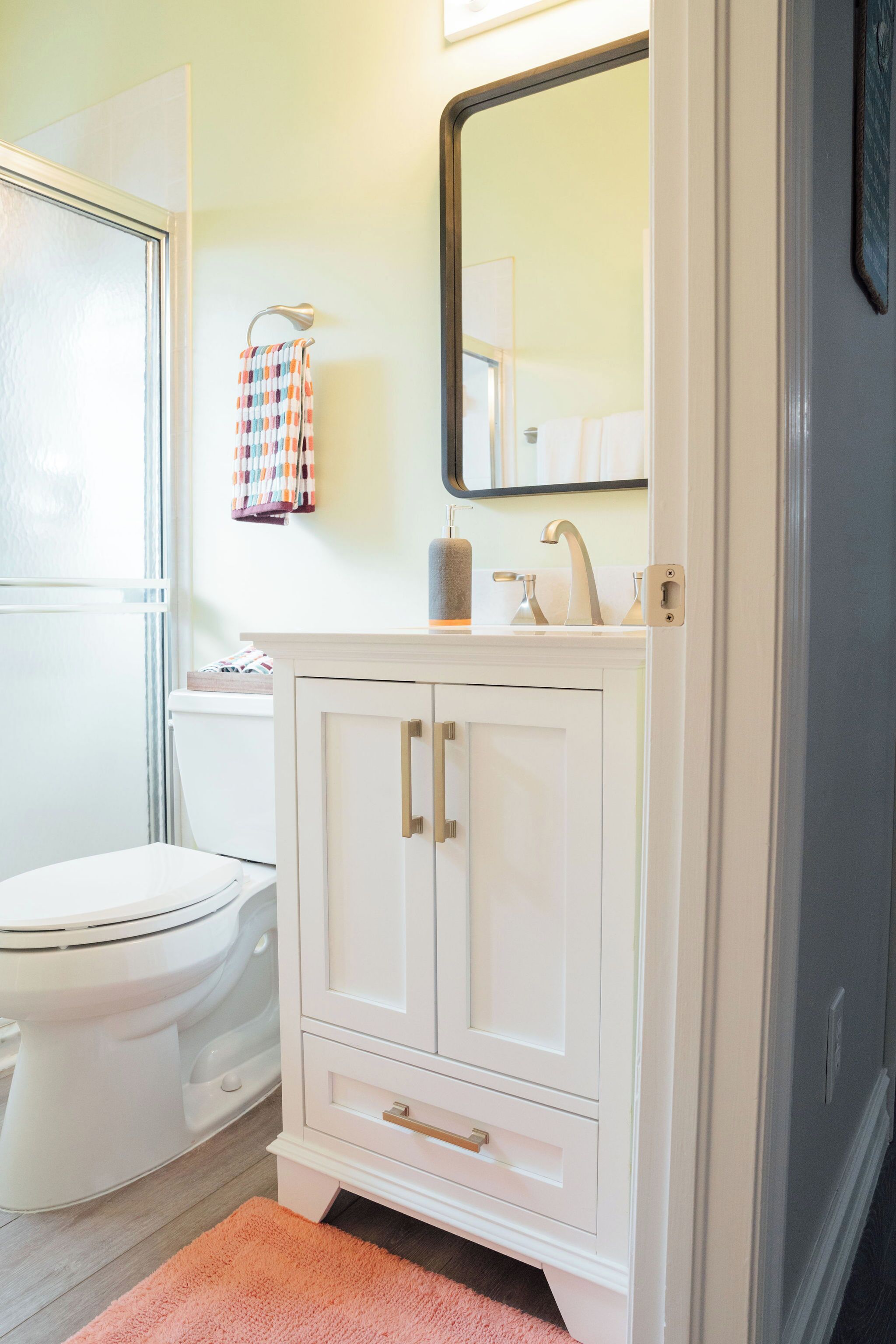 Et badeværelse med et hvidt toilet, et hvidt toiletbord med spejl og en lyserød måtte.