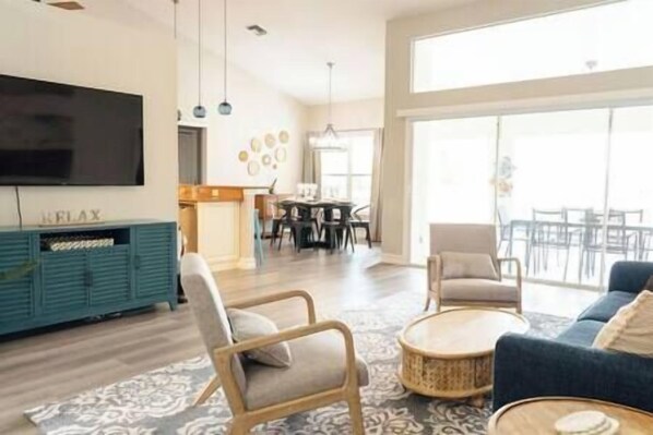 A spacious living room with a large TV, a dining area, and a balcony with outdoor seating.