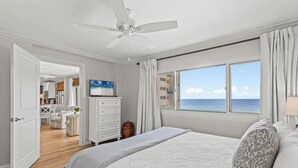 Een slaapkamer met een groot bed, een plafondventilator, uitzicht op de oceaan en een keuken op de achtergrond.