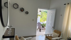 Una habitación moderna con muebles blancos, una mesa de centro de vidrio y una puerta que da a un espacio exterior con plantas.